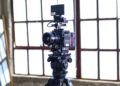 black filming camera on tripod near window