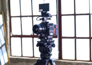 black filming camera on tripod near window